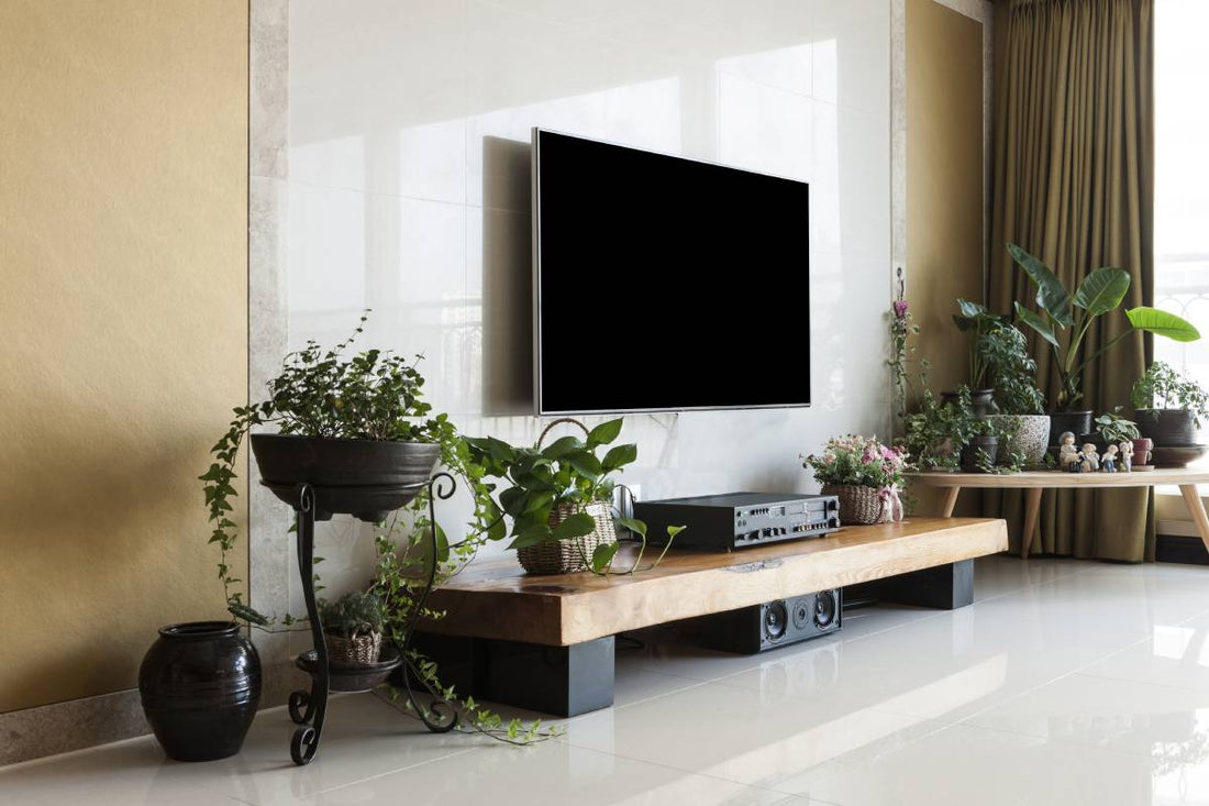 Living room with smart television, gold wall, white marble stone, wood table, audio, green plant pot, flower pot, picture.