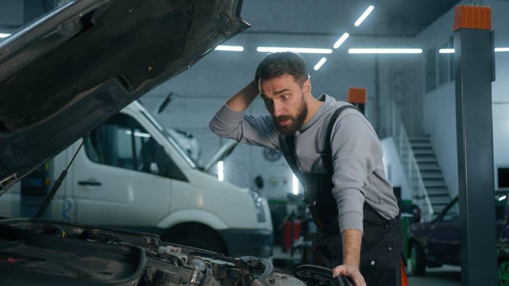 Male mechanic looking under the hood of a car with a surprised look on his face